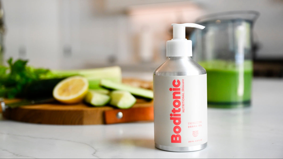 A bottle of Boditonic dietary supplement with a white pump dispenser and silver bottle, set on a kitchen counter with a green juice pitcher and fresh ingredients in the background.